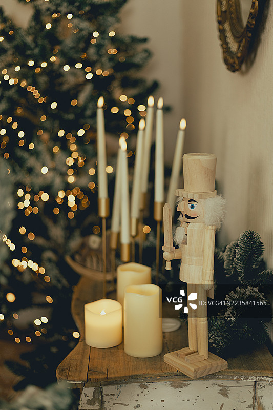 一个坚果夹站在燃烧的蜡烛和点亮的圣诞树旁，放在粗糙的木质表面上。图片素材