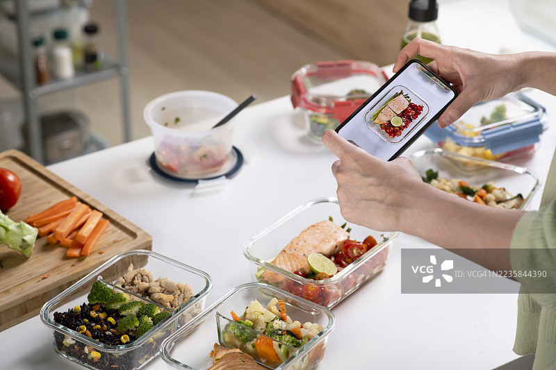 女性在家准备健康的自制餐，使用新鲜健康的食材。女性用智能手机拍照并制作健康餐的内容。图片素材