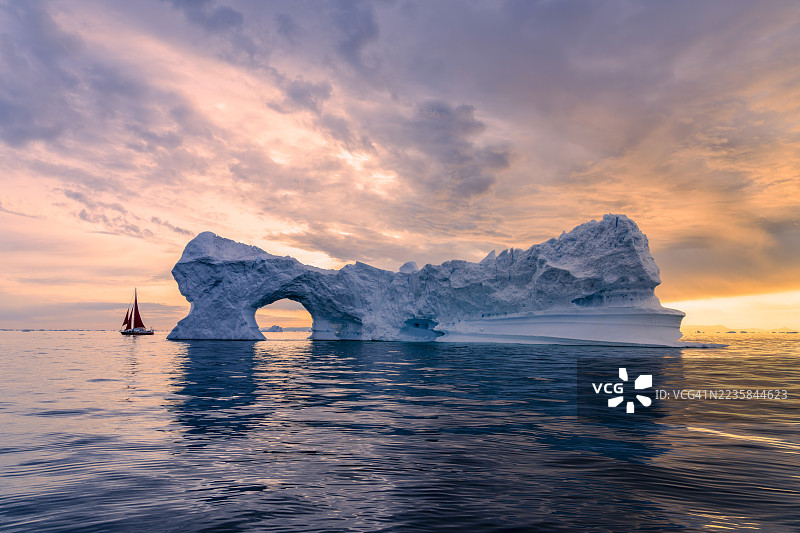 美丽的冰山拱门与红色帆船在夏季午夜阳光下的风景图片素材