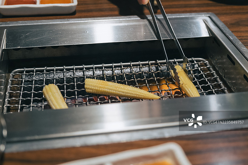 日式厨房或烧烤环境中，用金属夹子在明火上烤婴儿玉米图片素材