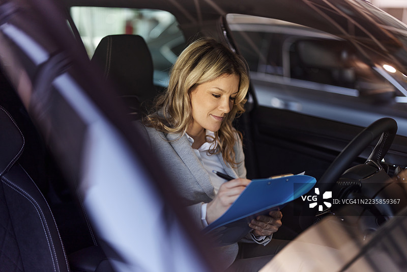 微笑的女销售员在展厅的汽车里做笔记。图片素材