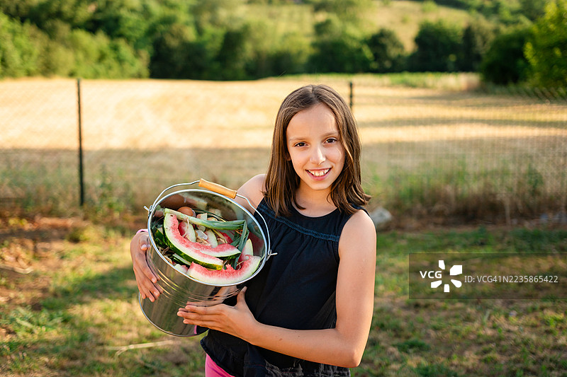 年轻女孩在田野里拿着一个金属堆肥桶图片素材