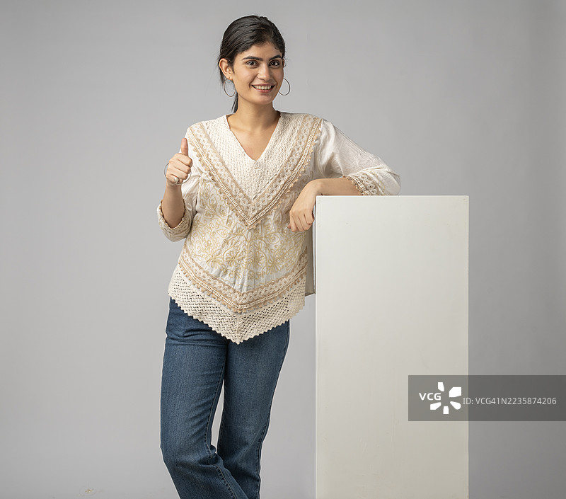 微笑的女性站在白色背景的空白块旁边图片素材