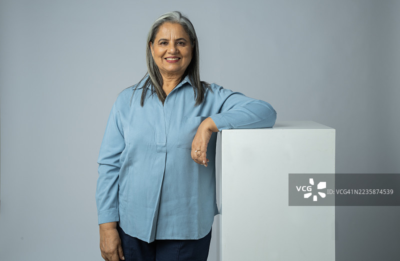 微笑的老年女性站在白色背景的空白块旁边图片素材