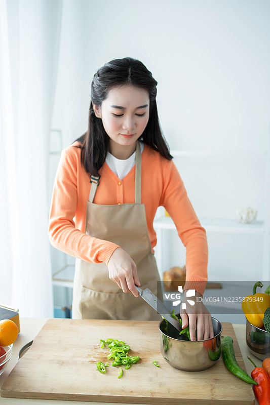 年轻女性穿着橙色上衣和围裙，在厨房里切青椒图片素材