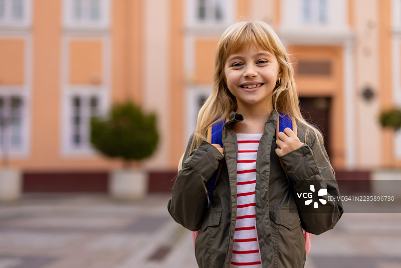 快乐的小女孩背着书包在小学前微笑图片素材