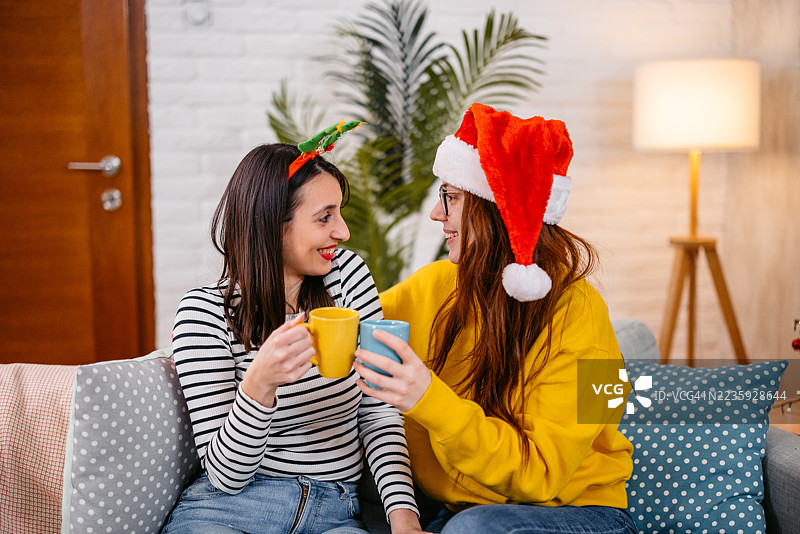 两个女性朋友在圣诞假期期间坐在沙发上喝咖啡聊天图片素材