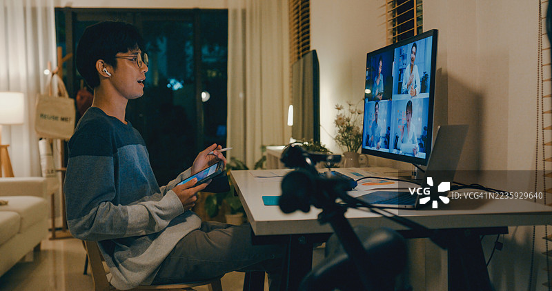 年轻的亚洲男子在家中的办公室里使用数字平板和笔记本电脑进行视频会议，展示远程工作和团队合作。远程办公与金融。图片素材