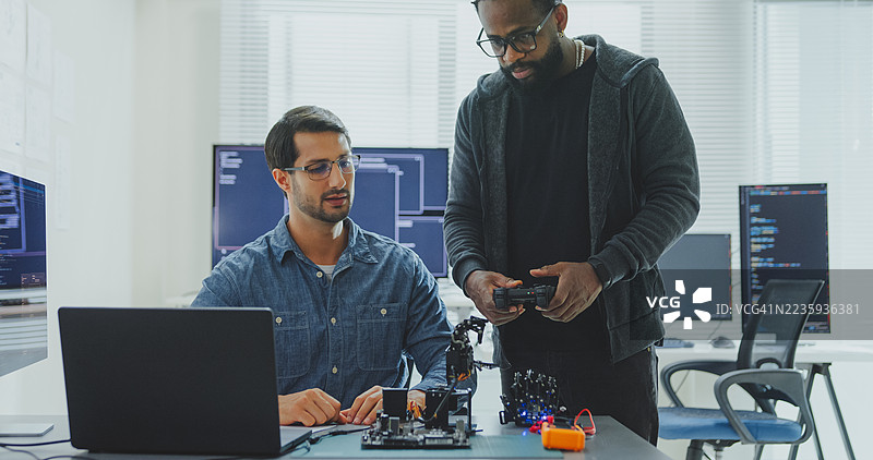 黑人和西班牙裔男性工程师程序员在科技办公室合作开发机器人手原型，使用计算机控制的机器人手臂电路。软件开发者，人工智能。图片素材