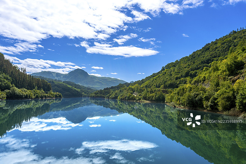 ibiur水库宁静的水面映照出湛蓝的天空和蓬松的白云,形成了一幅如画的景象,四周被托洛萨吉普斯夸的巴斯克山脉的翠绿山坡环绕。图片素材