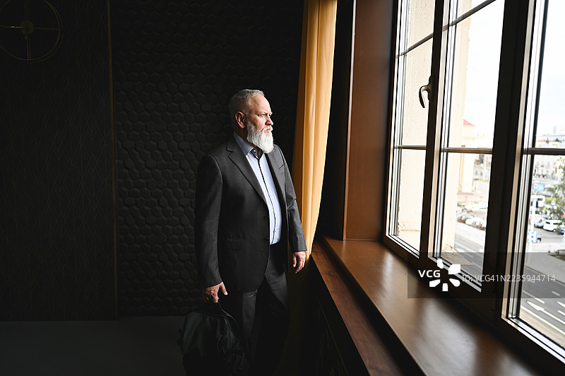 一位高级商人在昏暗的房间里望向窗外图片素材