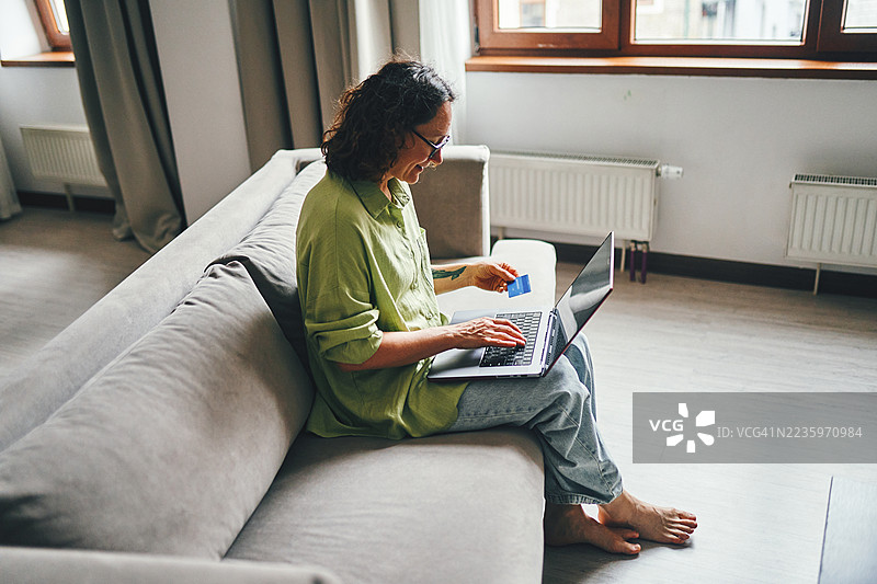 微笑的女性在明亮的客厅里用笔记本电脑在线购物图片素材