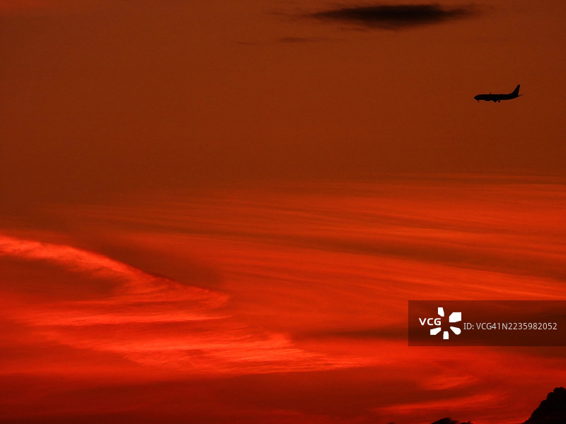 飞机在戏剧性的红橙色日落天空中飞行的剪影图片素材