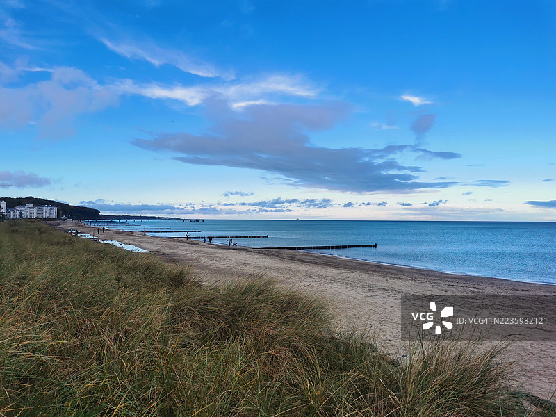 沙滩和海洋的美丽景色，蓝天白云下有防波堤，远处有建筑和海岸草地。图片素材