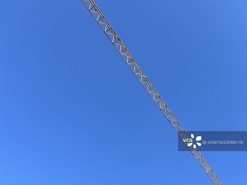 低角度视图的黄色起重机在阳光明媚的日子里与清澈的蓝天相映成趣，象征着建设与进步。图片素材