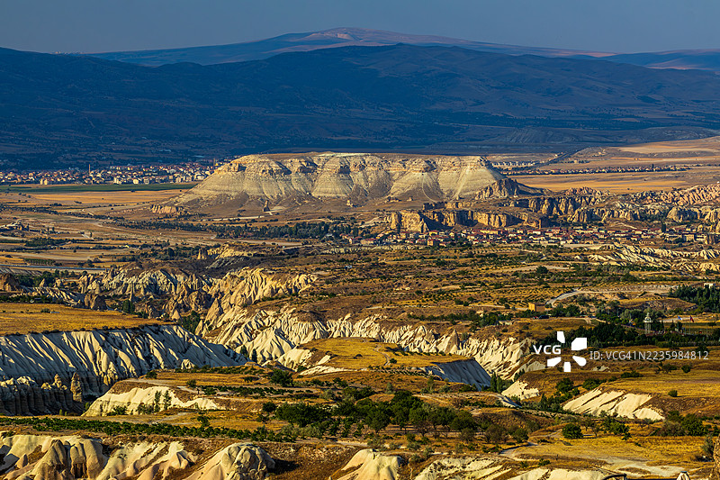 令人惊叹的空中视角，展现了广阔而崎岖的地貌，岩石形成和远处的村庄在晴朗的天空下。图片素材