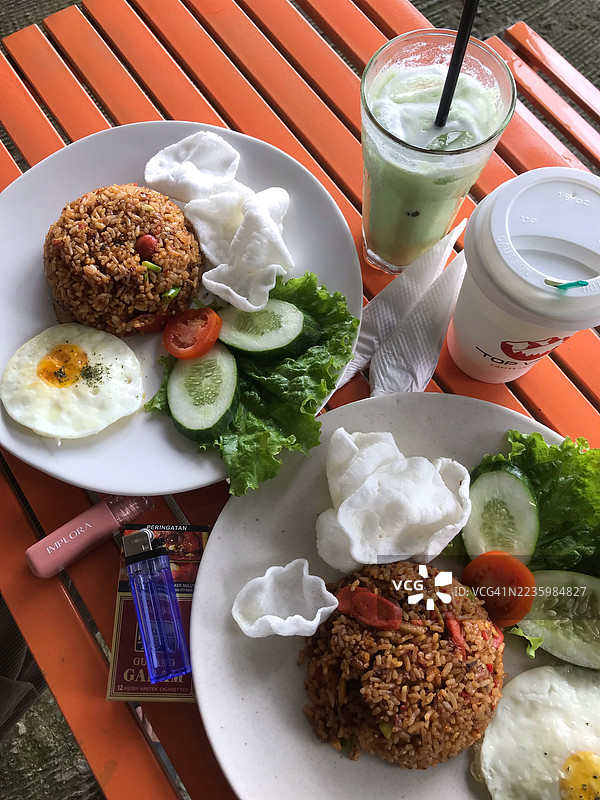 高角度视图，两盘炒饭配煎蛋、新鲜蔬菜和饮料，放在橙色条纹桌子上。图片素材