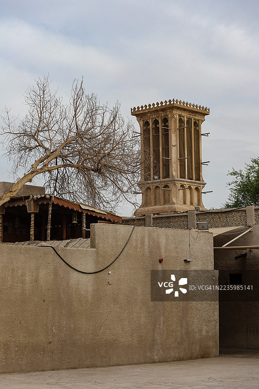 迪拜，阿拉伯联合酋长国的传统阿拉伯风塔和干旱树木在多云的天空下图片素材