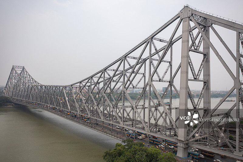 印度加尔各答的豪拉桥横跨胡格利河，繁忙的交通和城市天际线在灰色天空下。图片素材