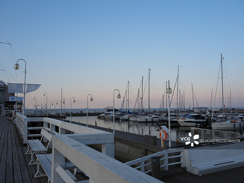 日落时分，波兰索波特的码头美景，停靠着众多游艇和帆船，木栈道上有长椅和路灯。图片素材