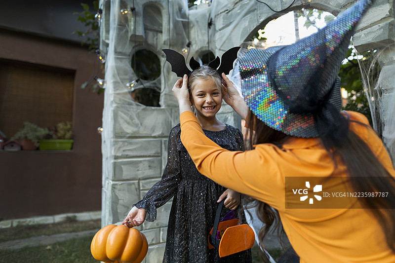 穿着闪亮蝙蝠服装的女孩与女巫在户外庆祝万圣节。图片素材