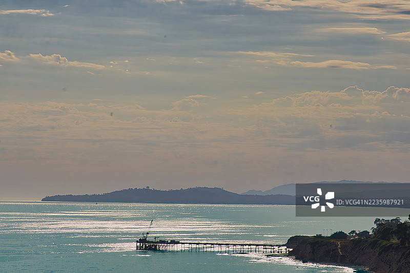 夕阳下，海边码头延伸入海，远方是云层密布的天空、远山和崎岖的海岸线，美国加州卡平特里亚图片素材