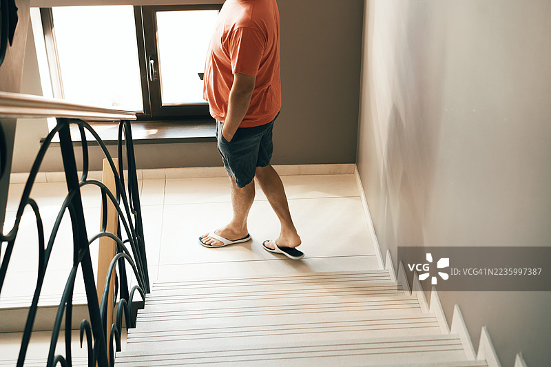 穿着休闲服和人字拖的男子在现代建筑内下楼梯图片素材