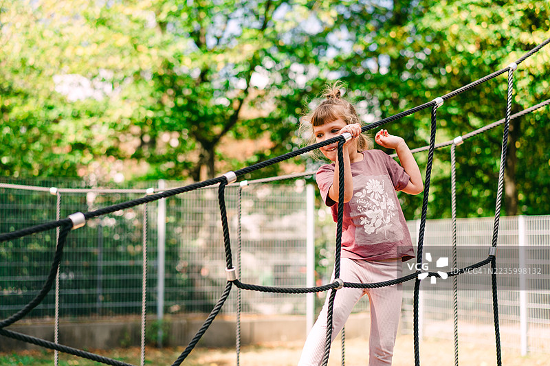 年轻女孩在户外公园的游乐设施上爬绳子图片素材