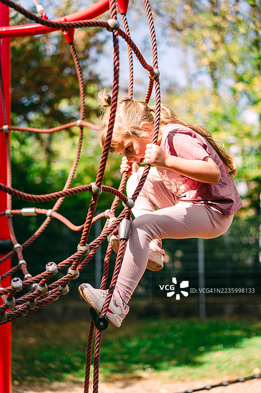 年轻女孩在户外公园的游乐设施上爬绳子图片素材