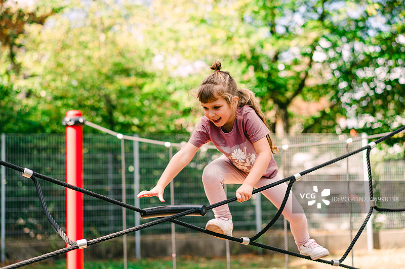 年轻女孩在户外公园的游乐设施上爬绳索图片素材
