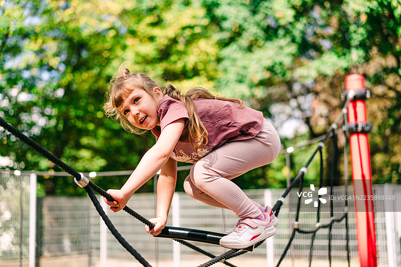 年轻女孩在户外公园的绳索游乐设施上攀爬图片素材
