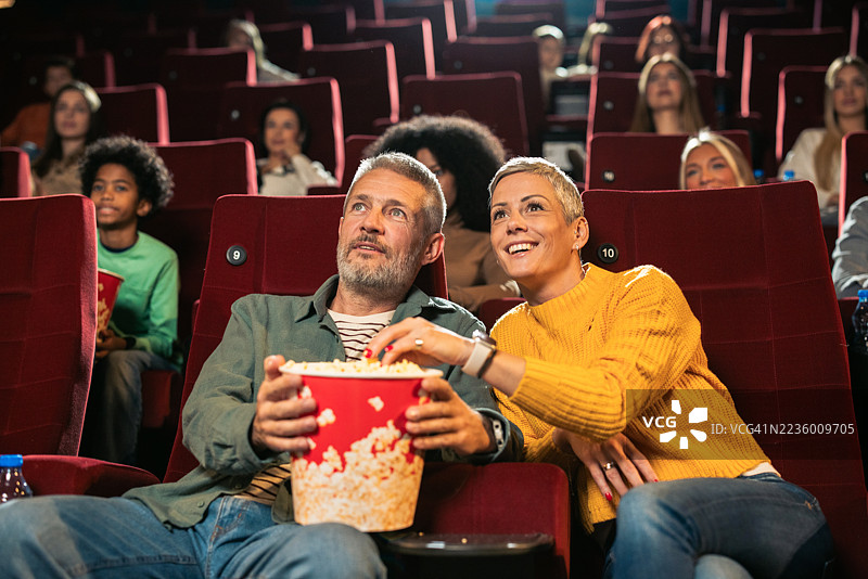快乐的情侣在电影院观看电影并吃爆米花图片素材