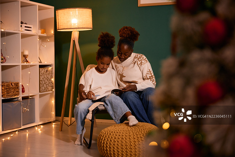 母亲和女儿在圣诞假期一起阅读一本书图片素材