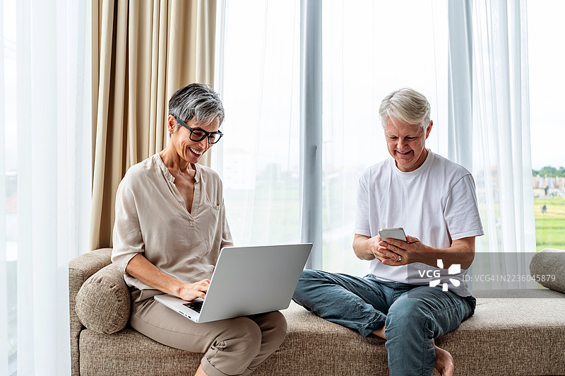 老年夫妇在家中享受使用笔记本电脑和智能手机的乐趣图片素材