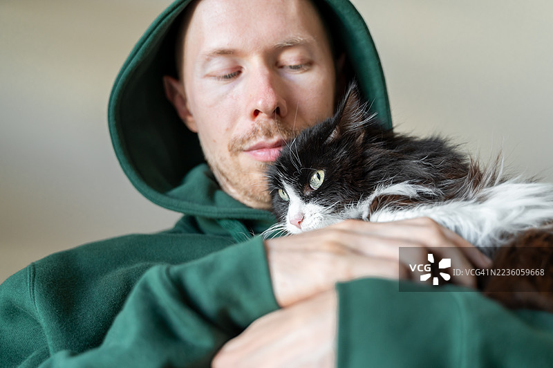 穿着绿色帽衫的秃头胡须男子抱着一只成年黑白猫图片素材