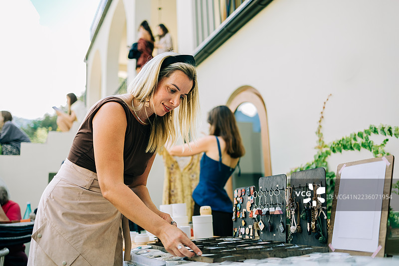 手工艺市场摊主在户外市场摊位上整理她的手工珠宝展示图片素材