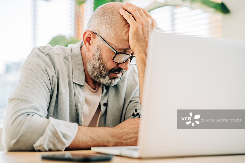 戴眼镜的中年男子近距离肖像，他正专注地看着笔记本电脑屏幕。象征深度专注和严肃思考。图片素材