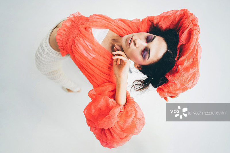 紫色眼妆的女子身着鲜艳的橙红色服装的俯视特写镜头。图片素材