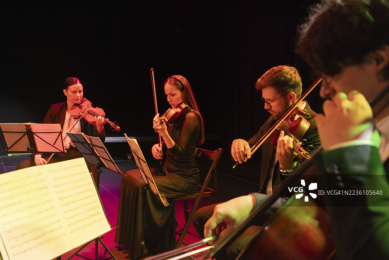 优雅的四重奏在昏暗的灯光下演奏古典音乐，专注的音乐家们。图片素材