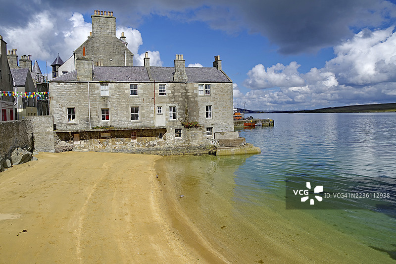 古老的石头小屋坐落在宁静的海滩上,清澈的海水和部分多云的天空,莱尔维克,设得兰群岛,苏格兰,英国图片素材