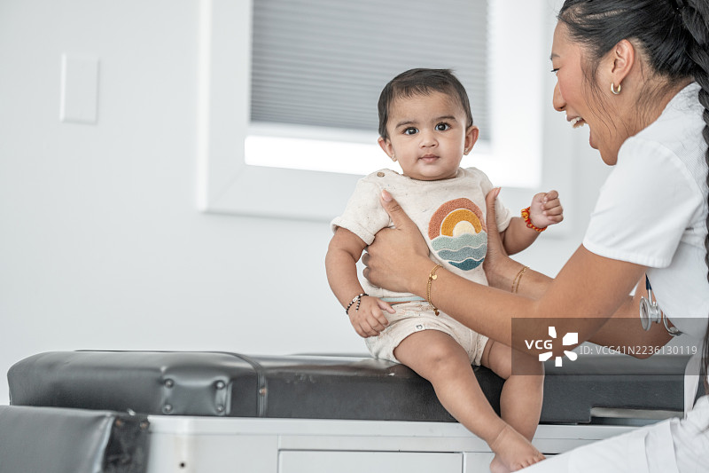 微笑的护士在明亮的诊所环境中协助婴儿进行常规健康检查图片素材