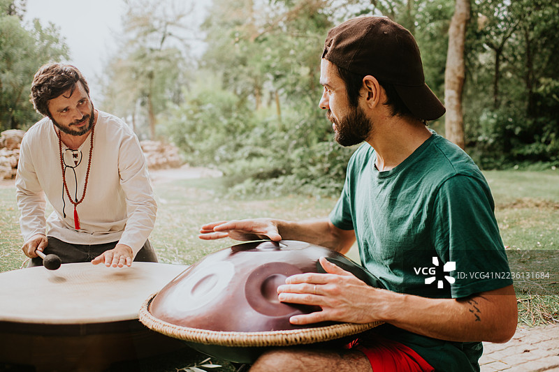 男人们在阳光明媚的户外环境中进行音乐会，演奏手盘和打击乐器图片素材
