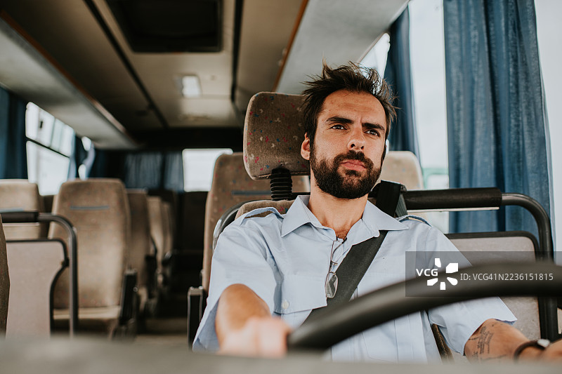 一位年轻的公交司机在白天驾驶一辆安静的客车，神情略显恼怒/专注。图片素材