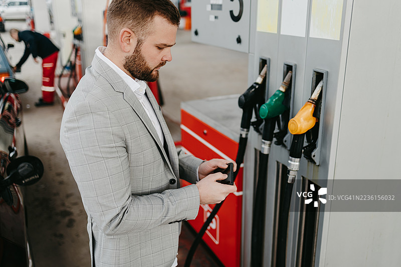 男子在加油站拿着手机选择燃料类型图片素材