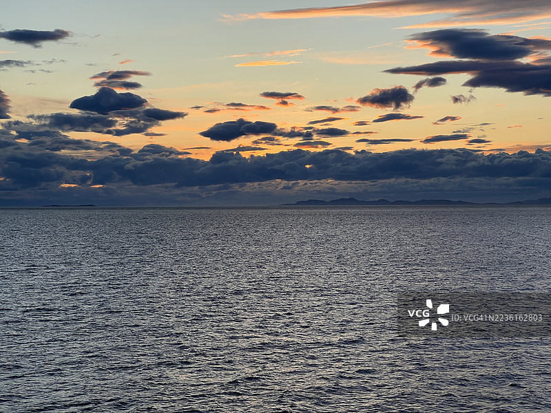 壮观的日落映照在辽阔的海洋上，天空多云，远处地平线上可见陆地轮廓，加拿大纳奈莫，纳努斯湾图片素材