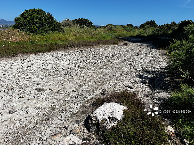 干裂的土地上长满绿色灌木，蓝天清澈，展现了干旱和环境变化，希腊图片素材