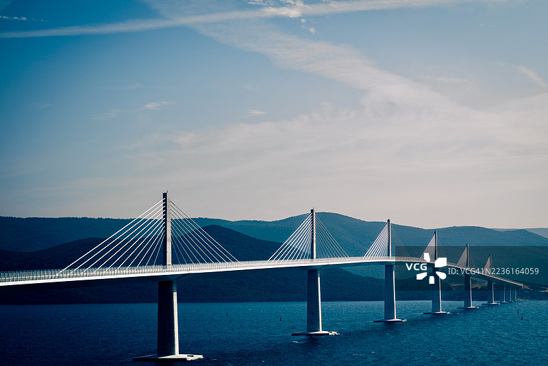 佩尔耶萨茨大桥横跨平静的海面，背景是蓝天和山脉。图片素材