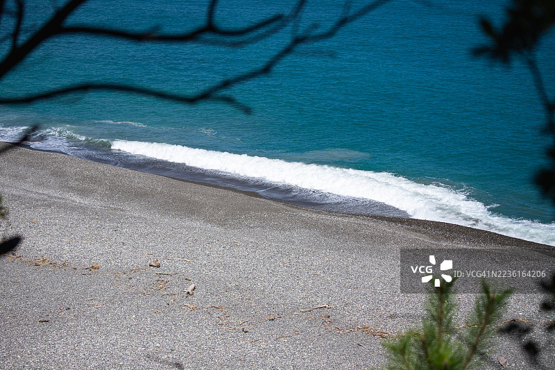 高角度视图的宁静卵石海滩，碧蓝的海水和拍打的浪花，树枝的剪影勾勒出画面，日本，新宫图片素材