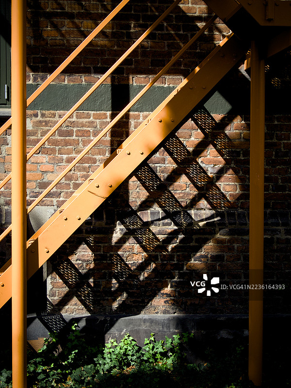 橙色金属楼梯上光影的抽象构图，背景是砖墙，底部有绿色常春藤，地点：丹麦奥胡斯图片素材