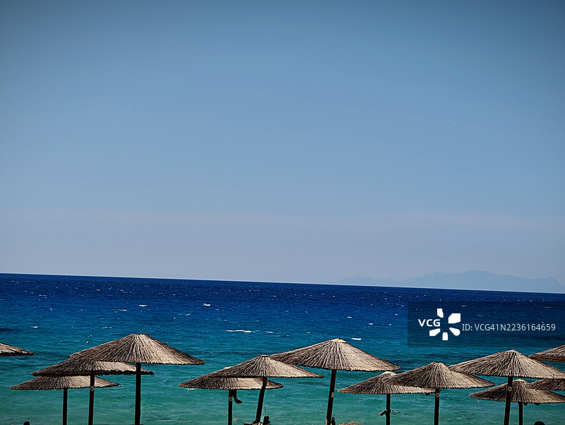 海滩的美丽景色，草编伞在清澈的蓝天和碧绿的海水映衬下。图片素材